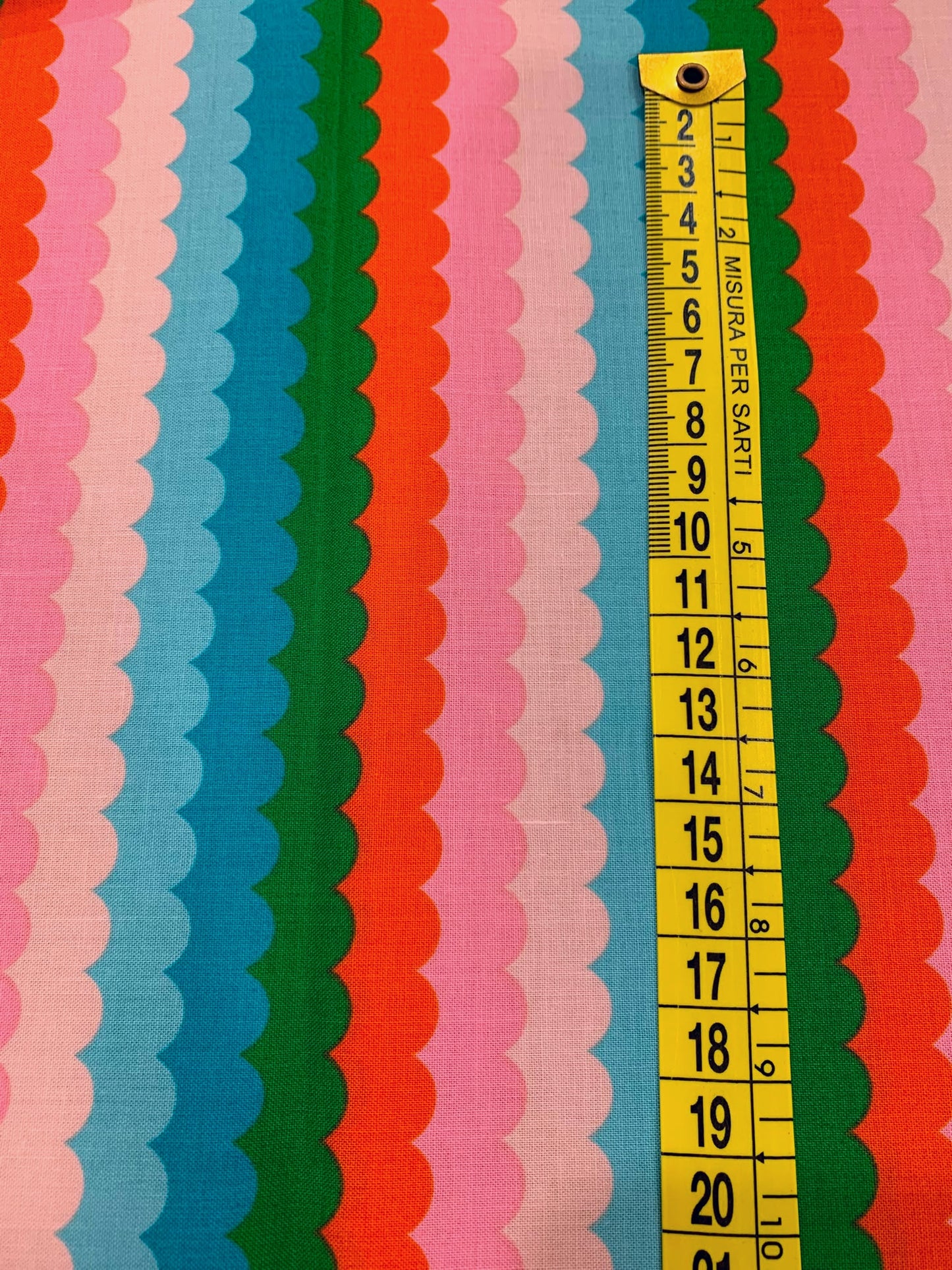 Dettaglio misura stampa tessuto cotone americano verde e arancione Poolside Too Scallops con stampe geometriche a onde retrò per cucito.