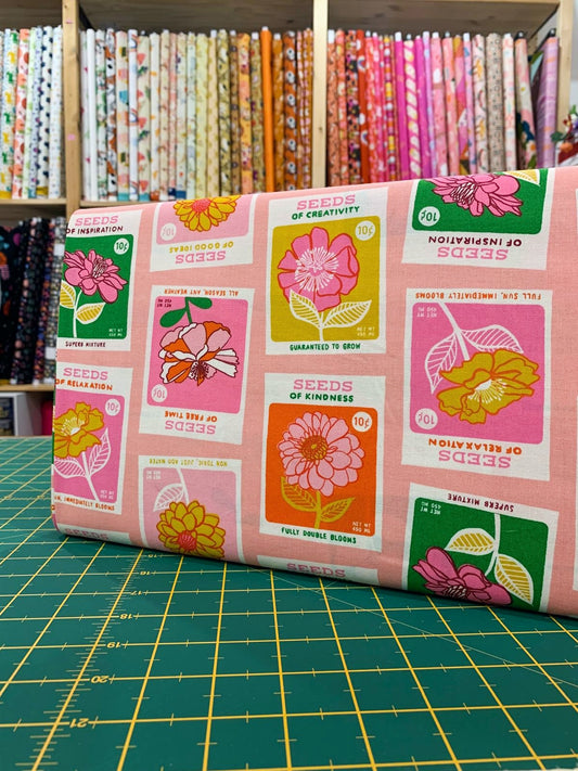 Tessuto cotone americano rosa Seeds Novelty Garden con stampe grafiche di bustine di semi vintage e scritte d'epoca per cucito creativo.